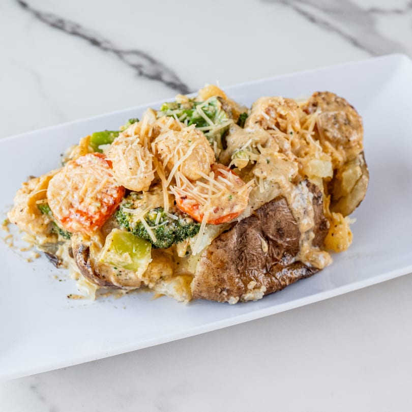 Baked potato topped with creamy sauce, chicken, broccoli, bell peppers, and shredded cheese.