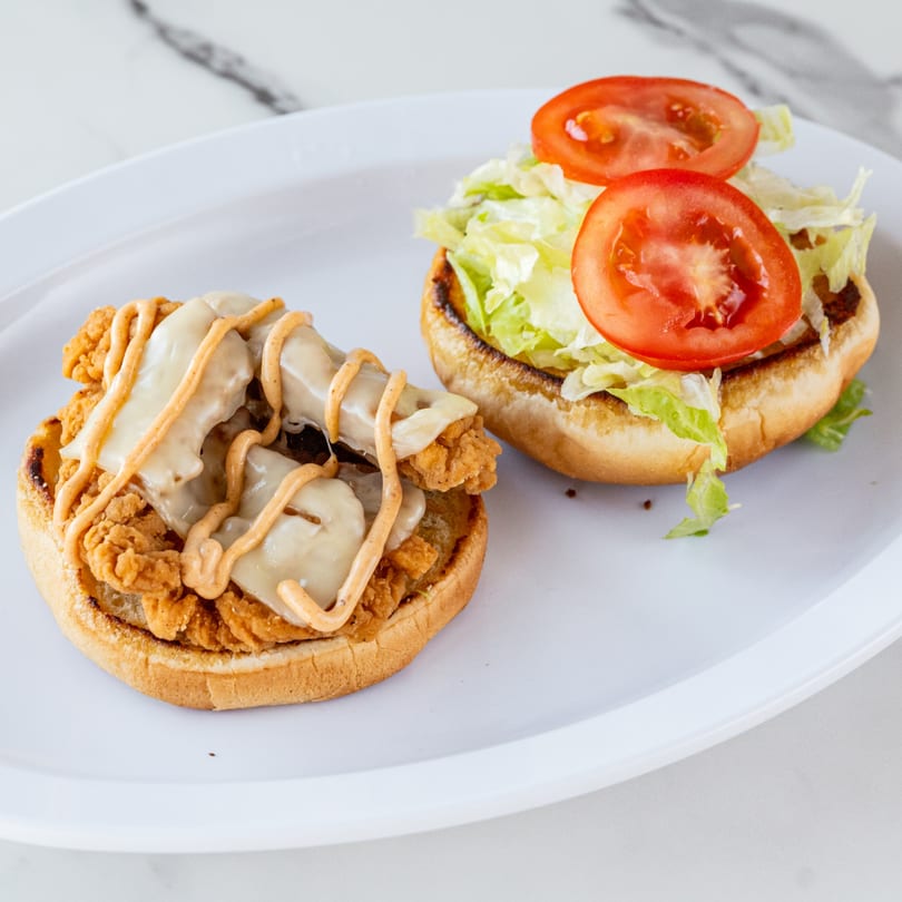 An open Urban Grill chicken sandwich with melted cheese, special sauce, lettuce, and tomato on a white plate.